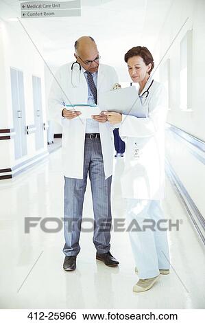 Doctors with medical charts consulting in hospital corridor View Large Photo Image Stock Photograph - Doctors with medical charts consulting in hospital corridor. Fotosearch