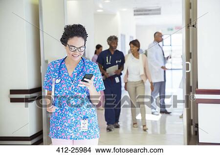 Picture - Nurse texting on cell phone in hospital corridor. Fotosearch