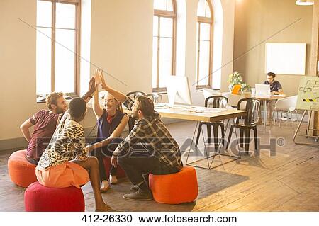 Stock Image - Casual business people joining hands in meeting in office. Fotosearch