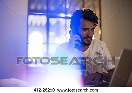 Stock Image - Casual businessman talking on cell phone at laptop. Fotosearch