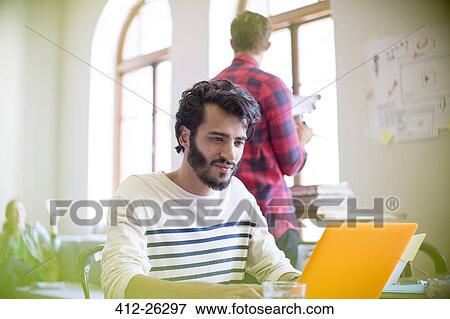 Casual businessman using laptop in office View Large Photo Image Stock Photo - Casual businessman using laptop in office. Fotosearch