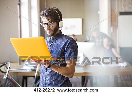Stock Image - Casual businessman wearing headphones and using laptop in office. Fotosearch