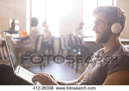 Casual businessman wearing headphones and working at laptop in office View Large Photo Image Stock Photo - Casual businessman wearing headphones and working at laptop in office. Fotosearch