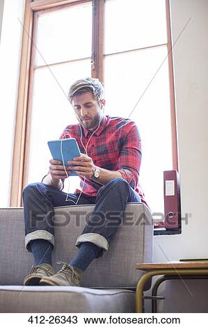 Stock Image - Casual businessman with headphones and digital tablet in office window. Fotosearch