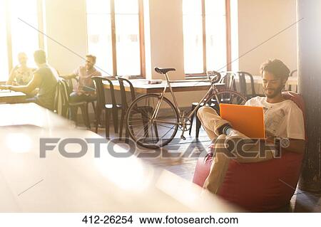 Picture - Casual businessman working at laptop in bean bag chair. Fotosearch