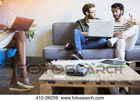 Stock Photo - Casual businessmen talking and using laptop on sofa. Fotosearch