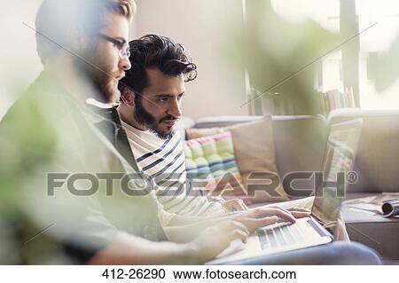 Stock Image - Casual businessmen working at laptop on sofa in office. Fotosearch