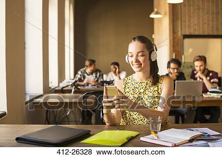 Casual businesswoman with headphones using cell phone in office View Large Photo Image Stock Photo - Casual businesswoman with headphones using cell phone in office. Fotosearch