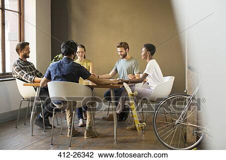Stock Image - Creative business people holding hands at table in meeting. Fotosearch