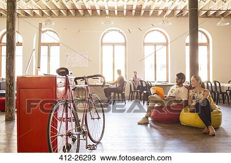 Stock Image - Creative business people using laptop on bean bag chairs in office. Fotosearch