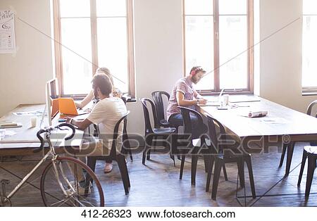 Stock Image - Creative business people working at tables in sunny office. Fotosearch
