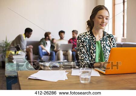 Stock Photograph - Creative businesswoman working at laptop with paperwork in office. Fotosearch