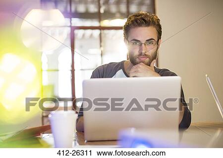 Stock Image - Focused casual businessman working at laptop in office. Fotosearch