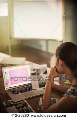 Stock Image - Focused creative businesswoman working at laptop and reviewing photographs. Fotosearch