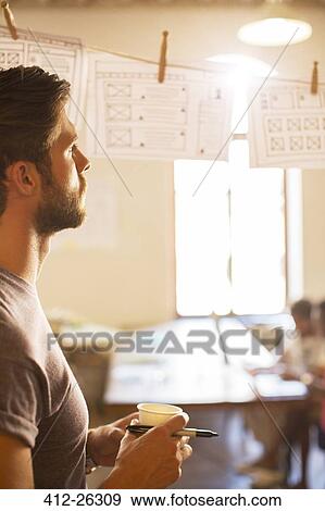 Pensive casual businessman reviewing hanging diagrams in office View Large Photo Image Stock Photo - Pensive casual businessman reviewing hanging diagrams in office. Fotosearch