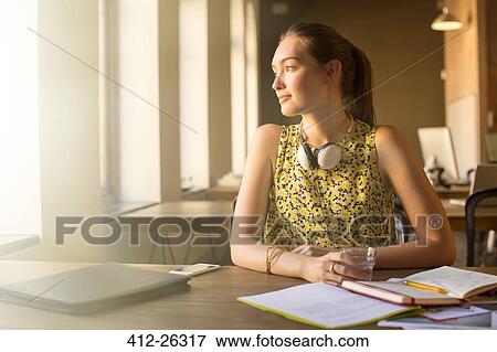 Stock Photo - Pensive casual businesswoman with headphones looking away in office. Fotosearch