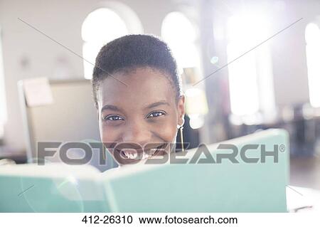 Stock Image - Portrait smiling businesswoman behind book in office. Fotosearch