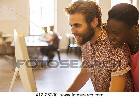 Smiling casual business people sharing computer in office View Large Photo Image Stock Image - Smiling casual business people sharing computer in office. Fotosearch