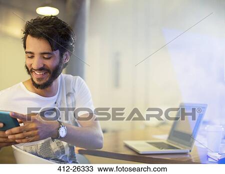 Smiling casual businessman texting with cell phone in office View Large Photo Image Stock Image - Smiling casual businessman texting with cell phone in office. Fotosearch