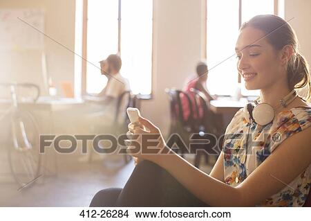 Picture - Smiling casual businesswoman texting on cell phone in office. Fotosearch