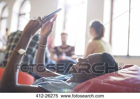 Stock Photography - Smiling casual businesswoman using digital tablet in bean bag chair. Fotosearch