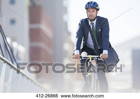 Businessman in suit and helmet riding bicycle in city View Large Photo Image Stock Photograph - Businessman in suit and helmet riding bicycle in city. Fotosearch
