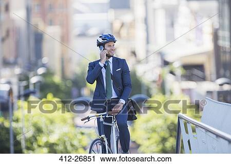 Businessman in suit and helmet sitting on bicycle talking on cell phone in city View Large Photo Image Stock Image - Businessman in suit and helmet sitting on bicycle talking on cell phone in city. Fotosearch