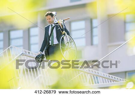 Businessman in suit carrying bicycle in city View Large Photo Image Stock Photo - Businessman in suit carrying bicycle in city. Fotosearch