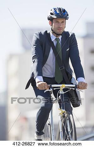 Stock Photo - Businessman in suit commuting on bicycle with helmet. Fotosearch