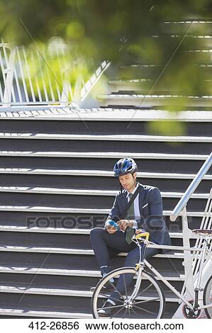 Businessman with helmet and bicycle texting with cell phone on urban stairs View Large Photo Image Stock Photograph - Businessman with helmet and bicycle texting with cell phone on urban stairs. Fotosearch