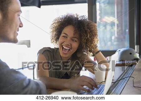 Stock Image - Enthusiastic woman laughing at laptop in cafe. Fotosearch