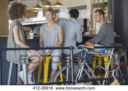 Stock Photograph - Friends hanging out talking and drinking coffee on cafe patio. Fotosearch