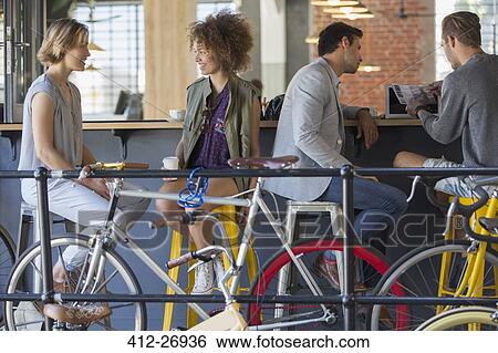 Stock Photograph - Friends hanging out talking and drinking coffee at cafe patio with bicycles. Fotosearch
