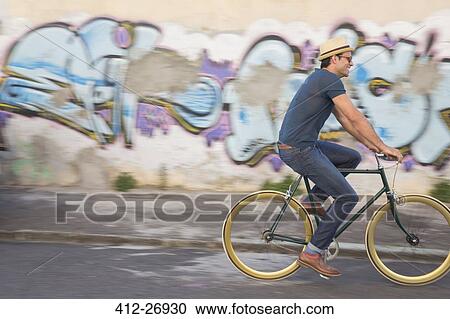 Hipster man riding bicycle on road along urban graffiti wall View Large Photo Image Stock Image - Hipster man riding bicycle on road along urban graffiti wall. Fotosearch