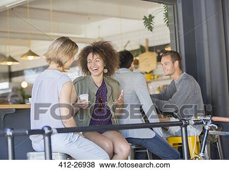 Laughing friends hanging out drinking coffee on cafe patio View Large Photo Image Stock Photo - Laughing friends hanging out drinking coffee on cafe patio. Fotosearch
