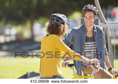 Man and woman with bicycles wearing helmets and talking in park View Large Photo Image Stock Photo - Man and woman with bicycles wearing helmets and talking in park. Fotosearch