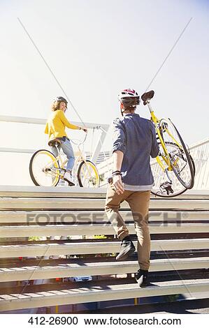 Man in helmet carrying bicycle up urban stairs View Large Photo Image Stock Image - Man in helmet carrying bicycle up urban stairs. Fotosearch