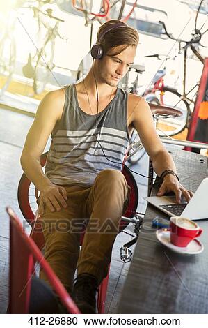 Stock Image - Man with headphones at laptop in cafe. Fotosearch