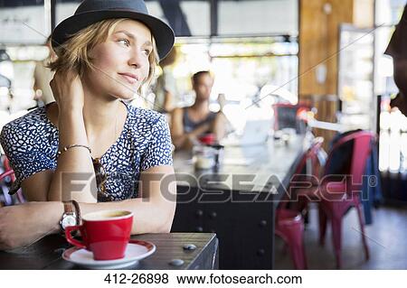 Stock Photo - Pensive woman in hat with coffee looking away in cafe. Fotosearch
