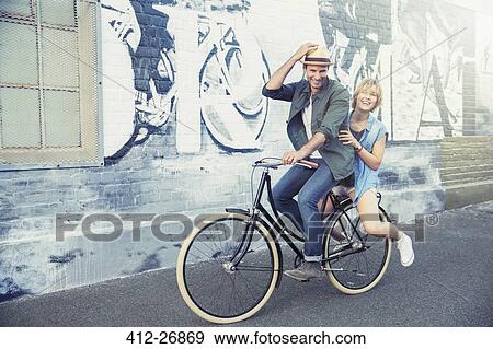 Portrait playful couple riding bicycle along urban graffiti wall View Large Photo Image Stock Photo - Portrait playful couple riding bicycle along urban graffiti wall. Fotosearch