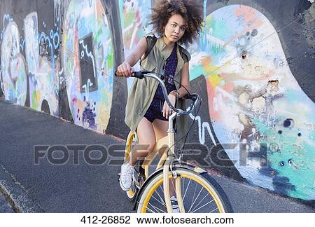 Portrait serious woman with afro on bicycle next to urban graffiti wall View Large Photo Image Stock Image - Portrait serious woman with afro on bicycle next to urban graffiti wall. Fotosearch