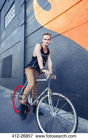 Portrait serious young man on bicycle next to urban graffiti wall View Large Photo Image Stock Photo - Portrait serious young man on bicycle next to urban graffiti wall. Fotosearch