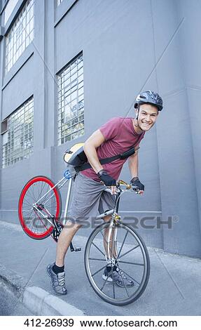 Stock Photo - Portrait smiling bicycle messenger with helmet leaning forward on urban sidewalk. Fotosearch