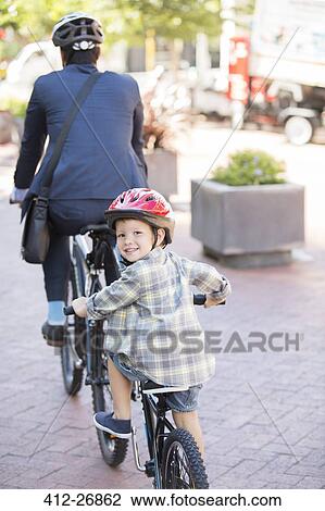 Stock Image - Portrait smiling boy riding tandem bicycle with businessman father. Fotosearch