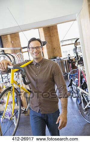 Stock Photo - Portrait smiling man with eyeglasses carrying bicycle in bicycle shop. Fotosearch