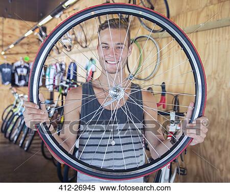 Portrait smiling young man holding bicycle wheel in bicycle shop View Large Photo Image Stock Photography - Portrait smiling young man holding bicycle wheel in bicycle shop. Fotosearch