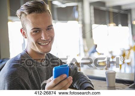 Portrait smiling young man texting with cell phone in cafe View Large Photo Image Picture - Portrait smiling young man texting with cell phone in cafe. Fotosearch