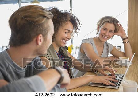 Stock Image - Smiling friends with laptop and coffee hanging out in cafe. Fotosearch