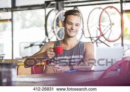 Smiling man drinking coffee at laptop in bike shop View Large Photo Image Stock Image - Smiling man drinking coffee at laptop in bike shop. Fotosearch