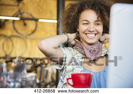 Smiling woman at laptop in bike shop adjusting neck scarf View Large Photo Image Stock Photo - Smiling woman at laptop in bike shop adjusting neck scarf. Fotosearch